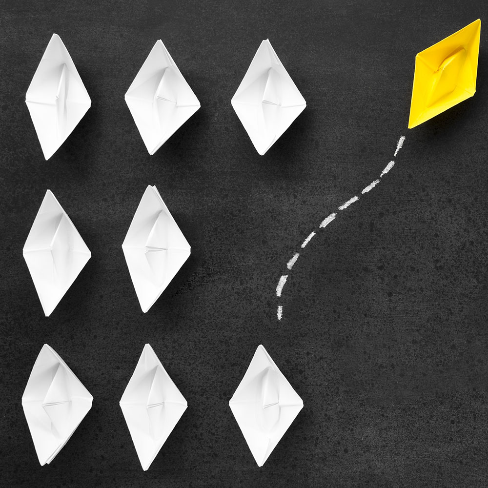 a yellow paper boar along with multiple white boats indicating standing out from crowd.